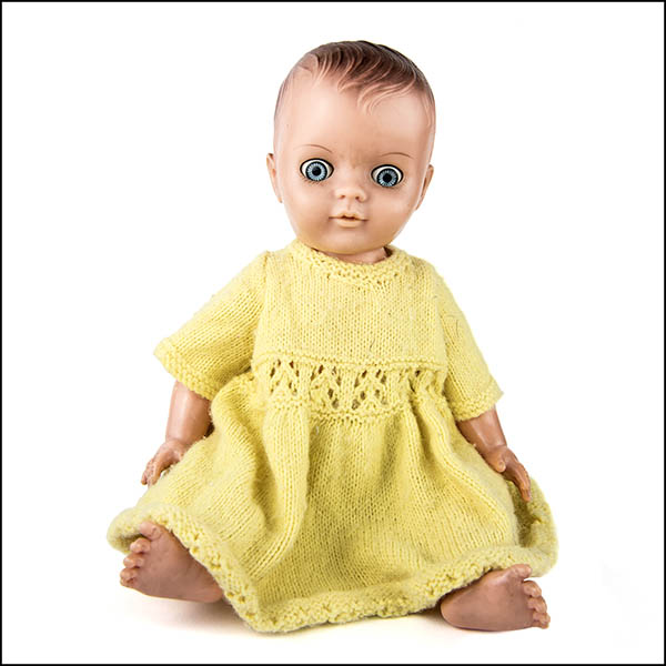 Vintage hard plastic doll with crazy eyes wearing a yellow knitted dress
