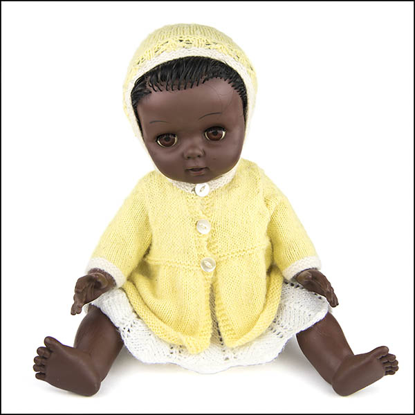 Vintage hard plastic doll wearing white knitted dress, yellow cardigan and bonnet